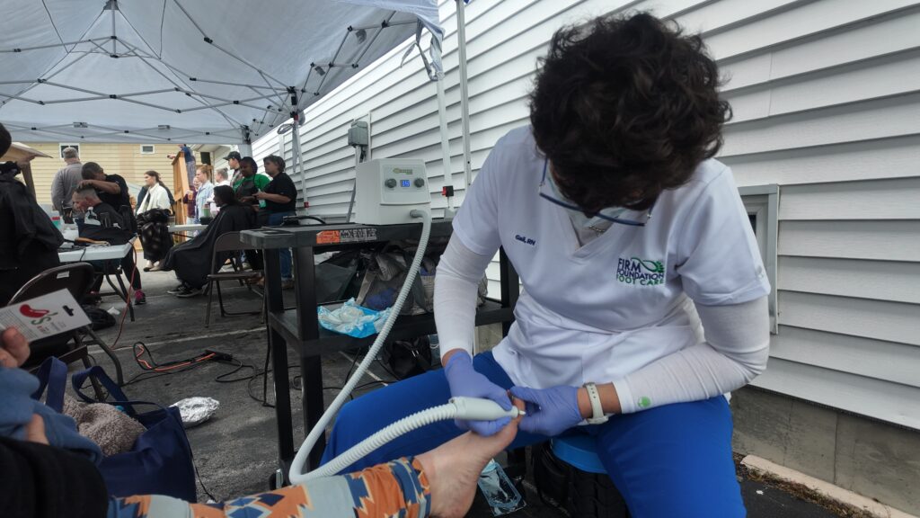 Gail Hackelberg volunteering at a Cuts 4 Christ community event, performing foot care services outdoors alongside other volunteers and hairstylists.